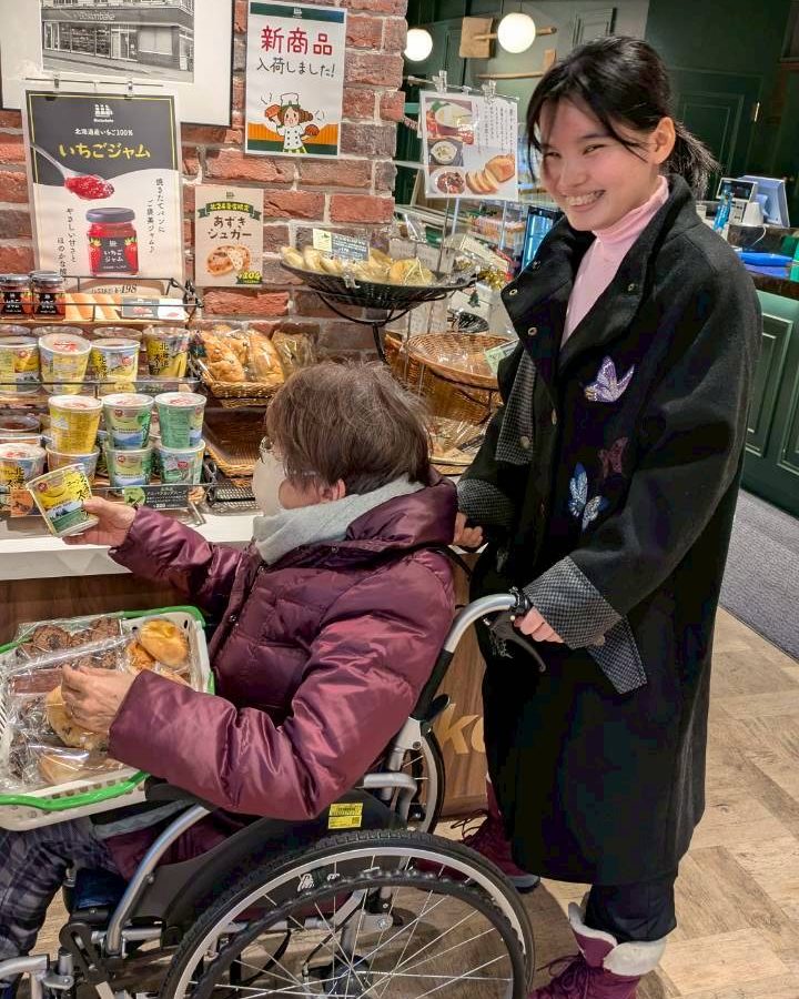 学生が車いすのシニアに付き添って、パン屋さんで買い物をしている様子