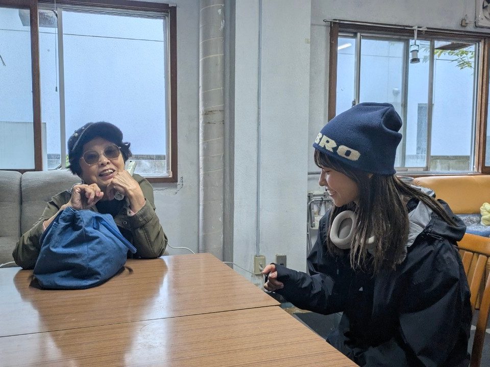 テーブル越しに、シニアの女性と学生が笑顔で話している様子