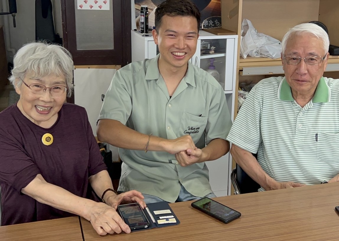 スマホ教室でシニアと学生が笑顔でフィストバンプする様子