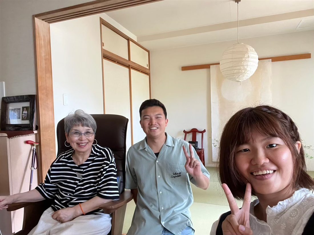 畳の部屋で、シニアの女性と学生2人がピースサインで写る様子