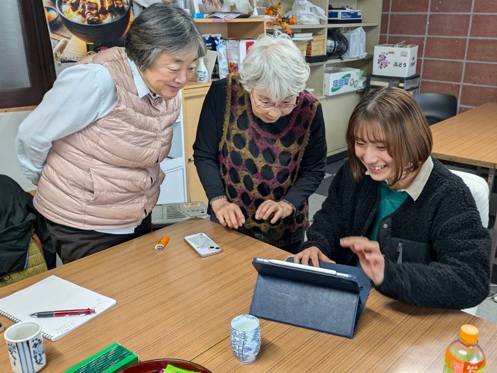 学生がタブレットを操作し、シニア2人が笑顔でのぞき込む様子