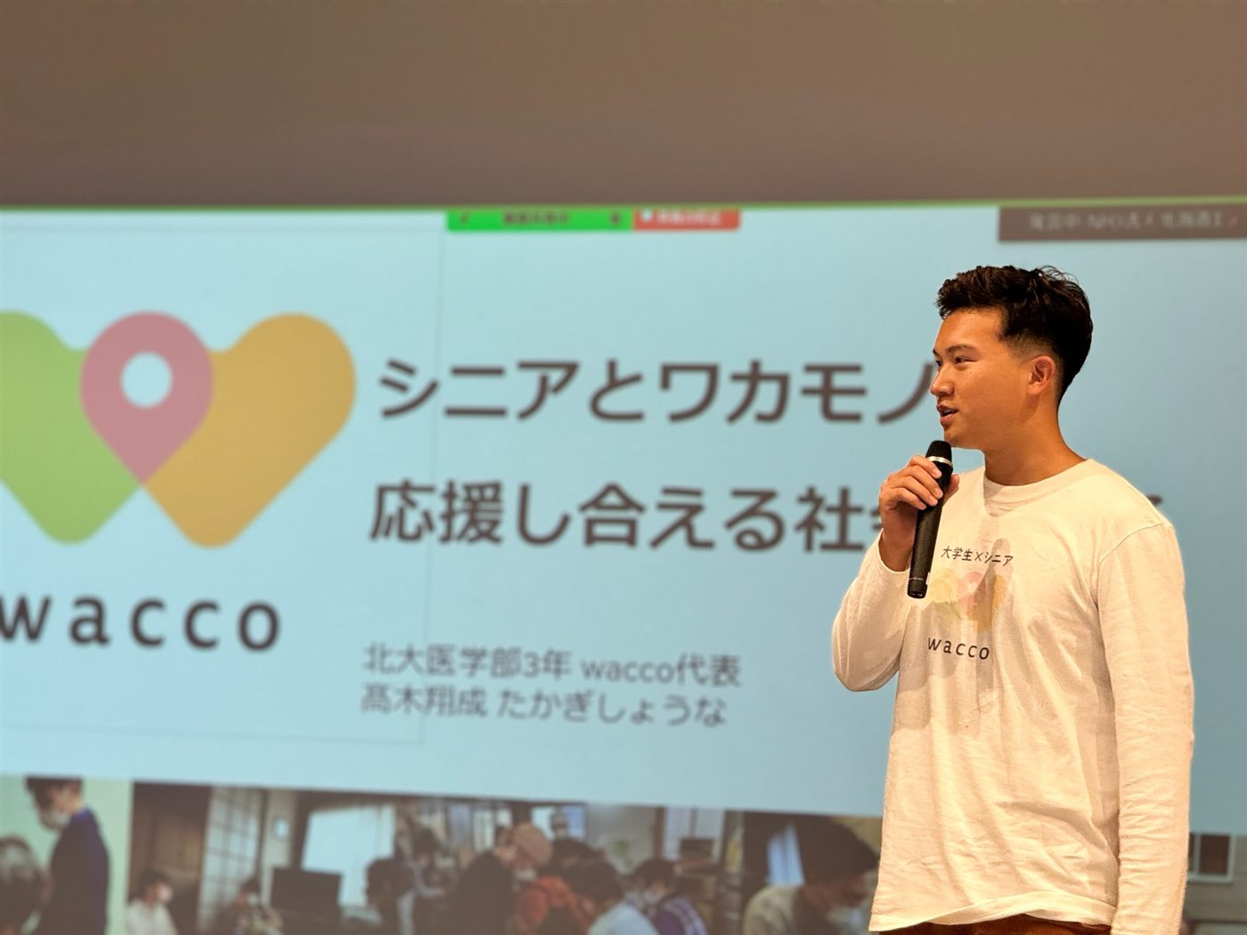 スライドの前でマイクを持って活動を紹介する様子